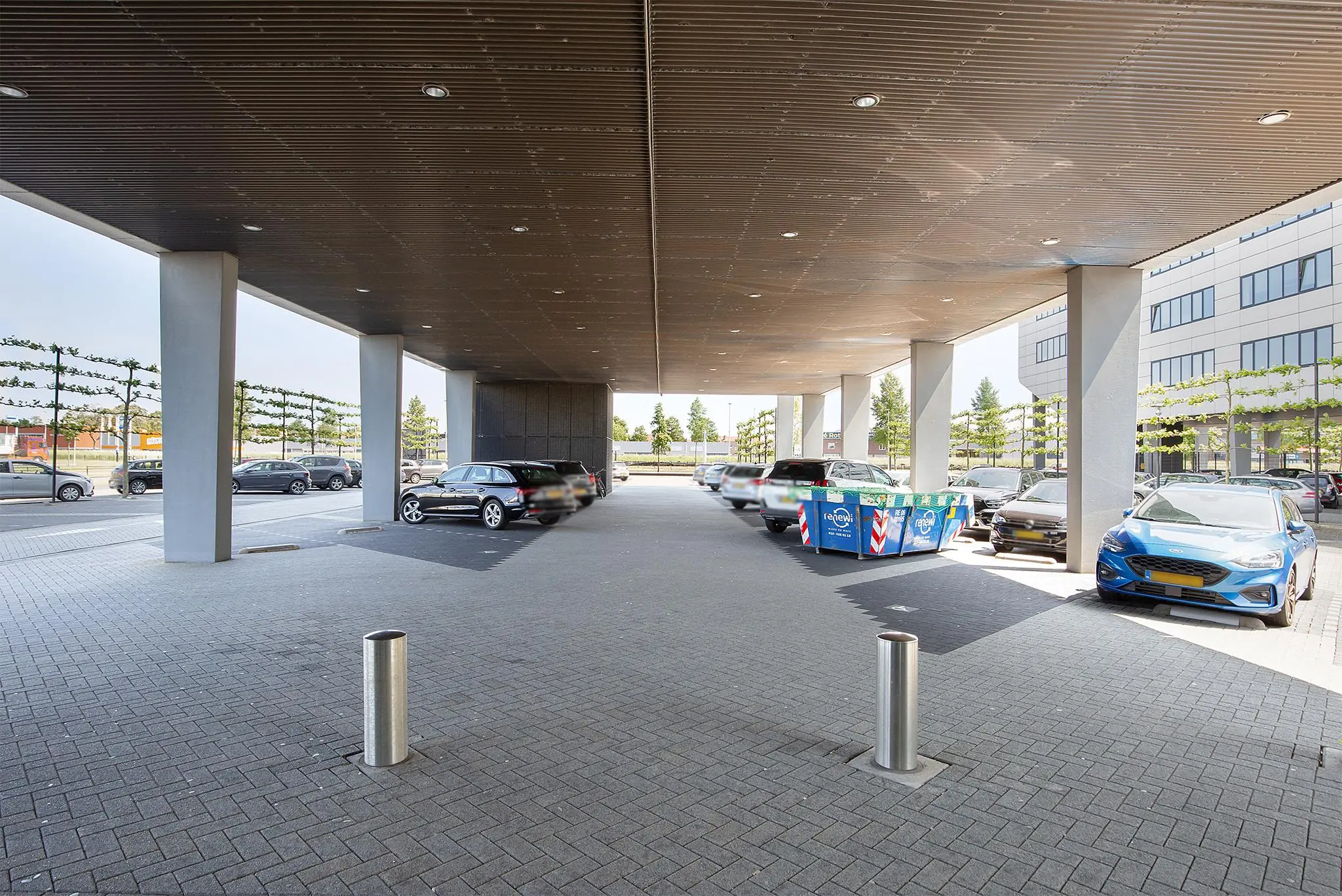 Overdekte parkeerruimte bij een modern kantoorpand aan de Waalhaven-Oostzijde, met geparkeerde auto’s en een bouwcontainer.